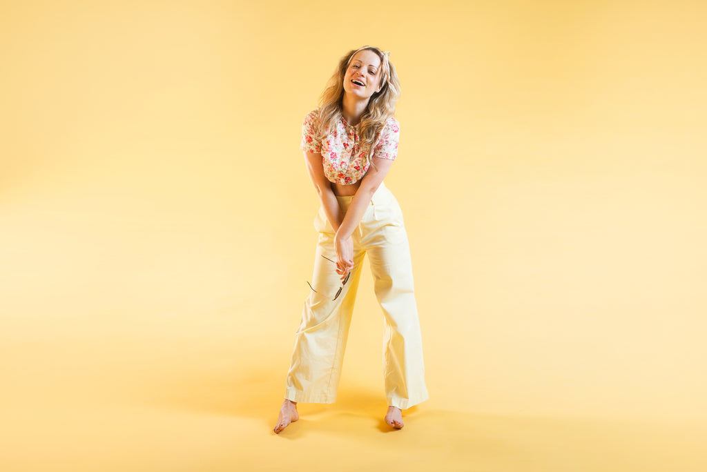 A woman dressed in chic casual wear, including a stylish blouse and high-waisted jeans. She poses in a bright