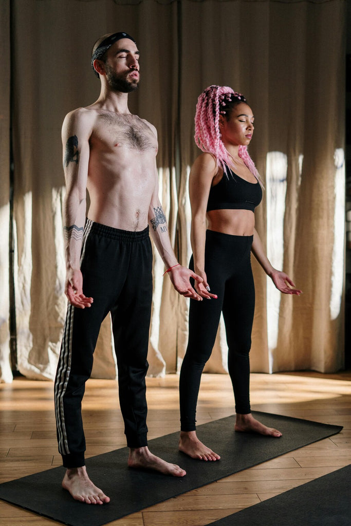 Two individuals practicing yoga on mats in a serene setting. One person is performing a warrior pose while the other is in a downward dog position.